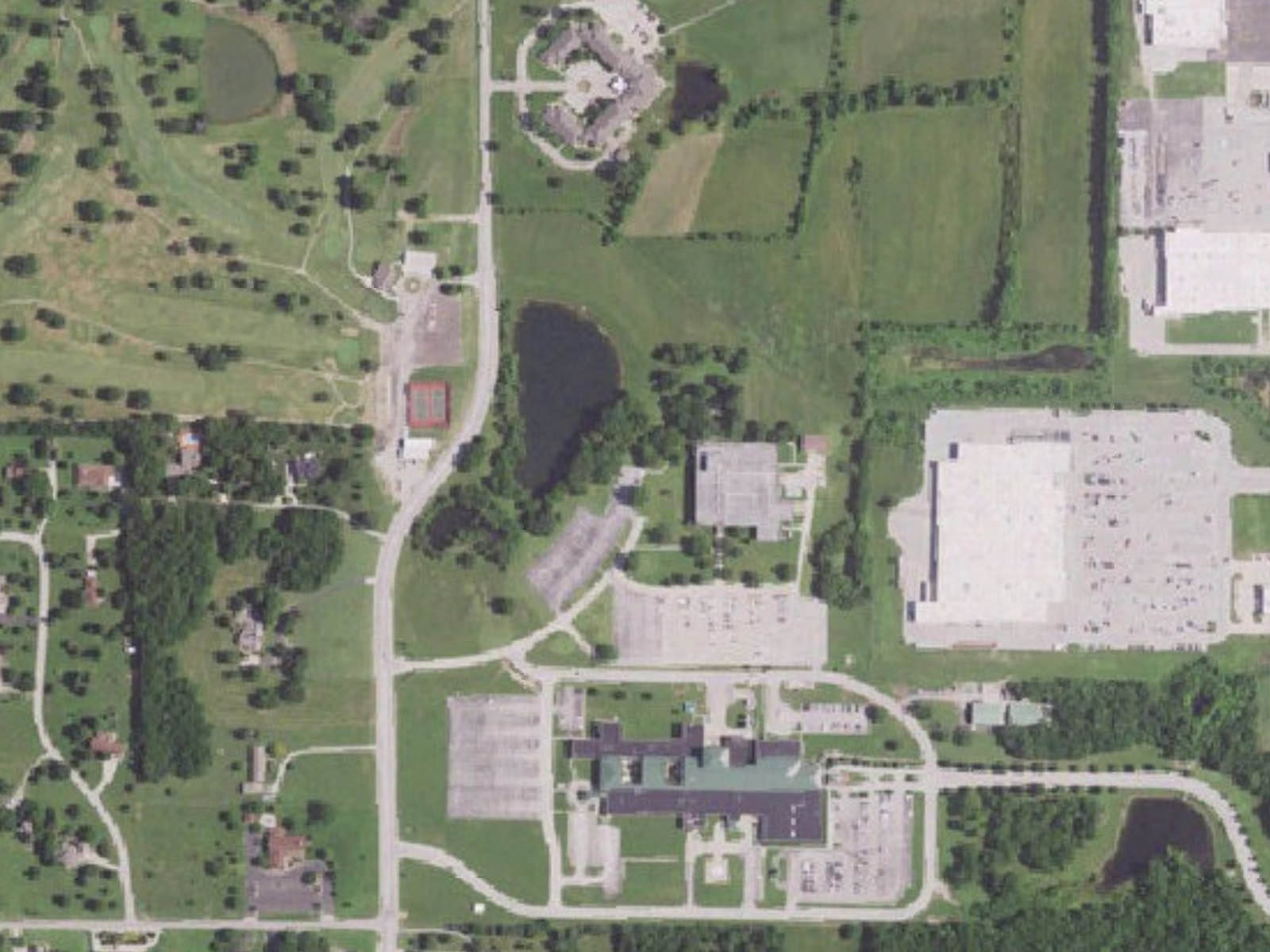 Aerial view of the site: the office building and its parking lot at center, a pond and open fields to the north, a golf course to the west across South Horton Street, and the former hospital campus to the south.